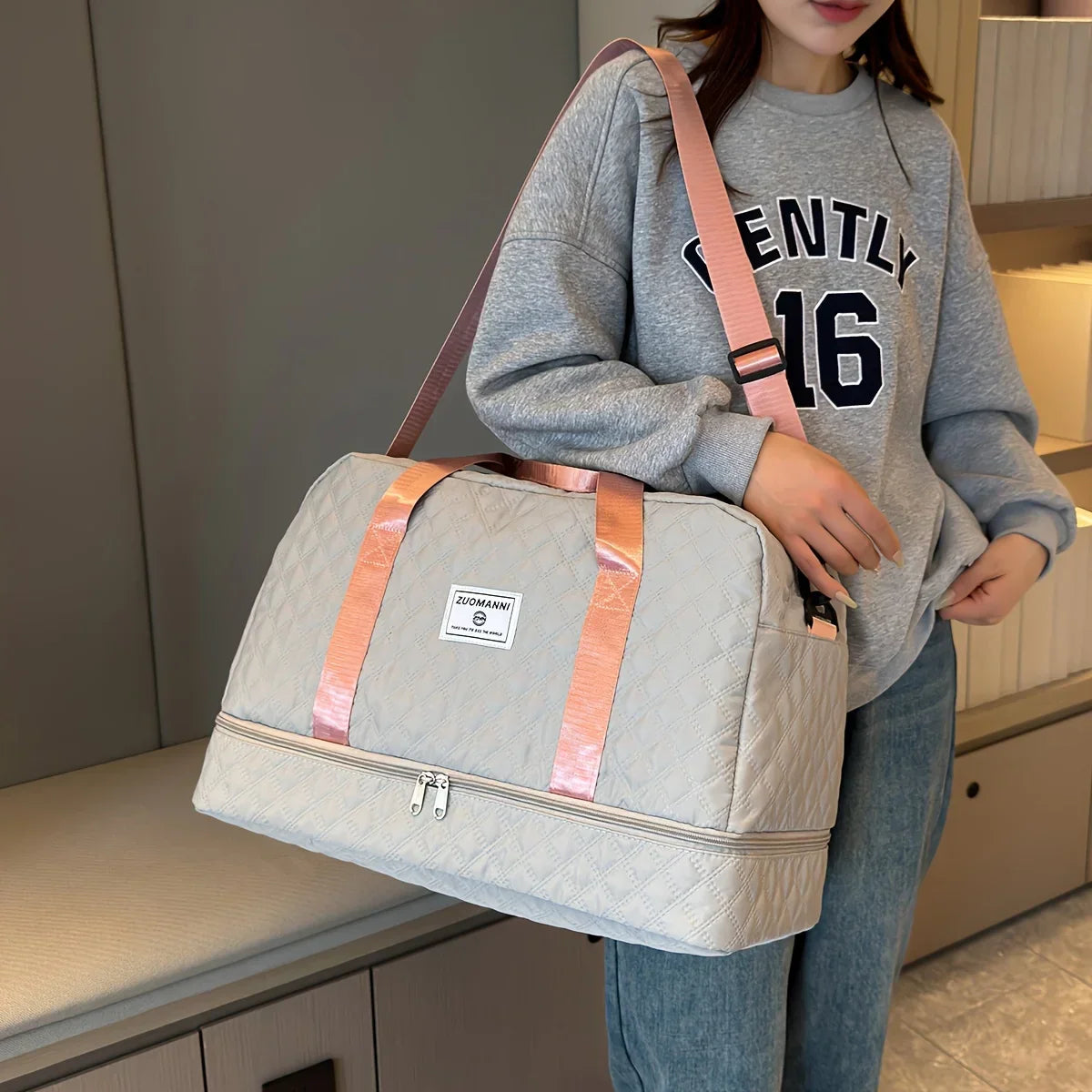 Woman wearing a grey sweatshirt with 'GENTLY 16', holding a quilted travel duffel bag with pink straps.