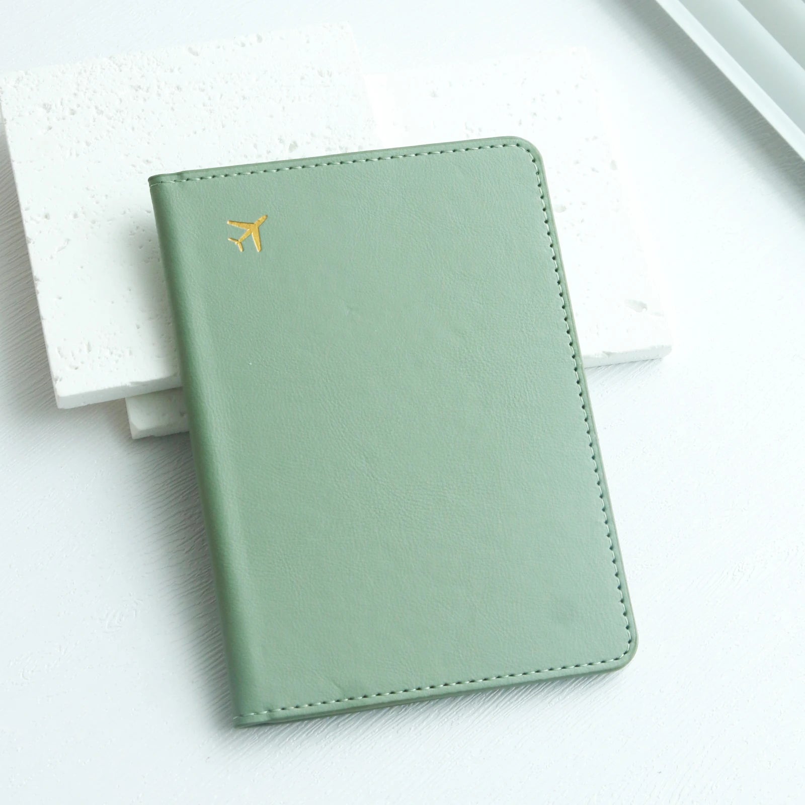 Minimalist mint green passport holder with gold airplane icon on white background, Elarose