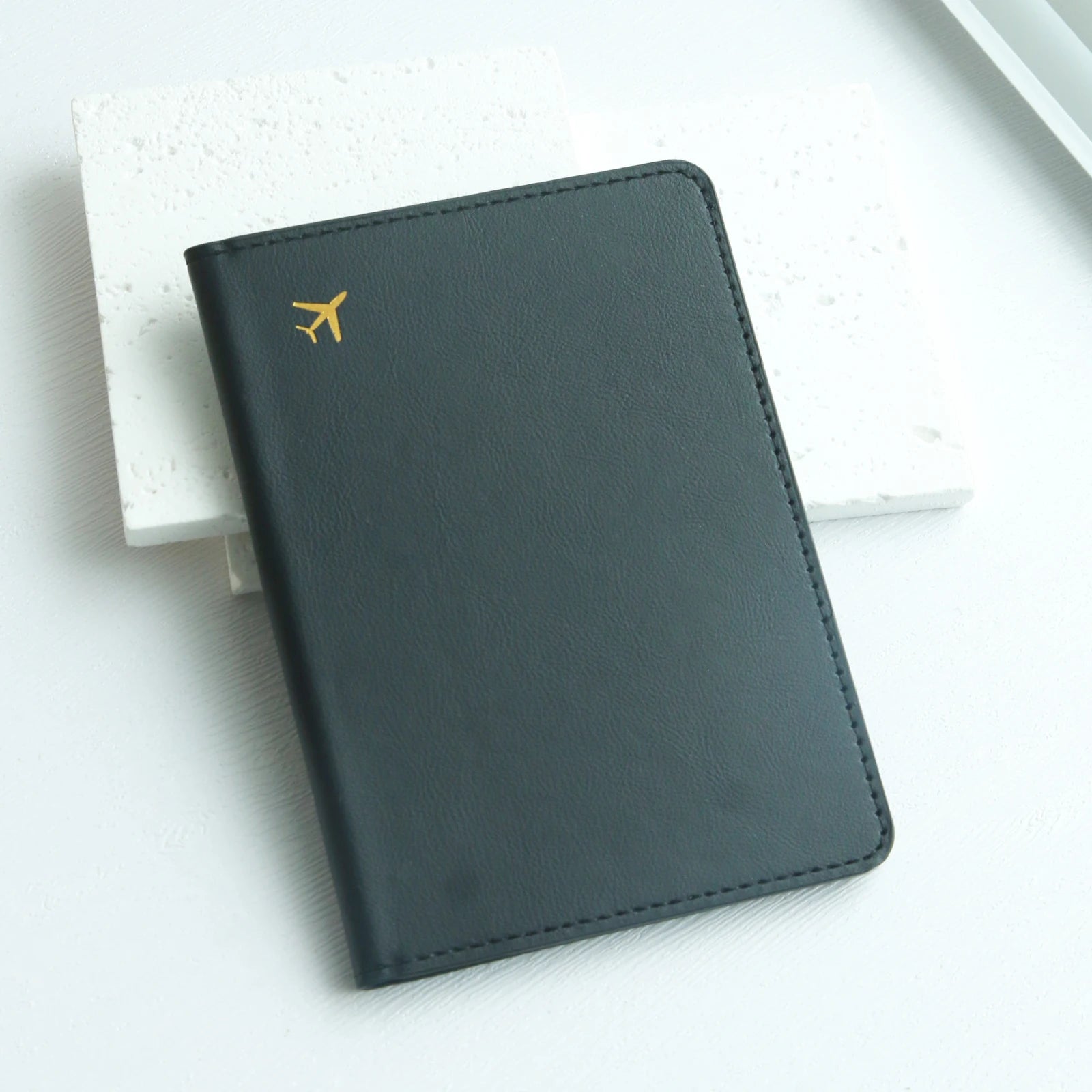 Black travel passport holder with gold airplane icon on white Elarose background