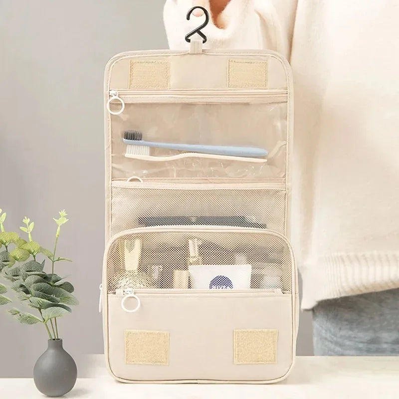 Beige hanging toiletry organizer with toiletries and toothbrush, on table near plant, Elarose