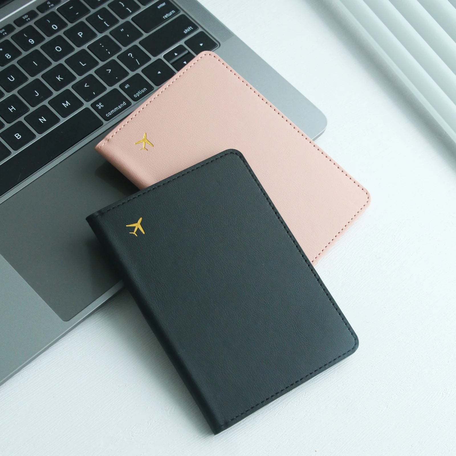 Black and pink Elarose leather passport holders on laptop keyboard with gold airplane icon