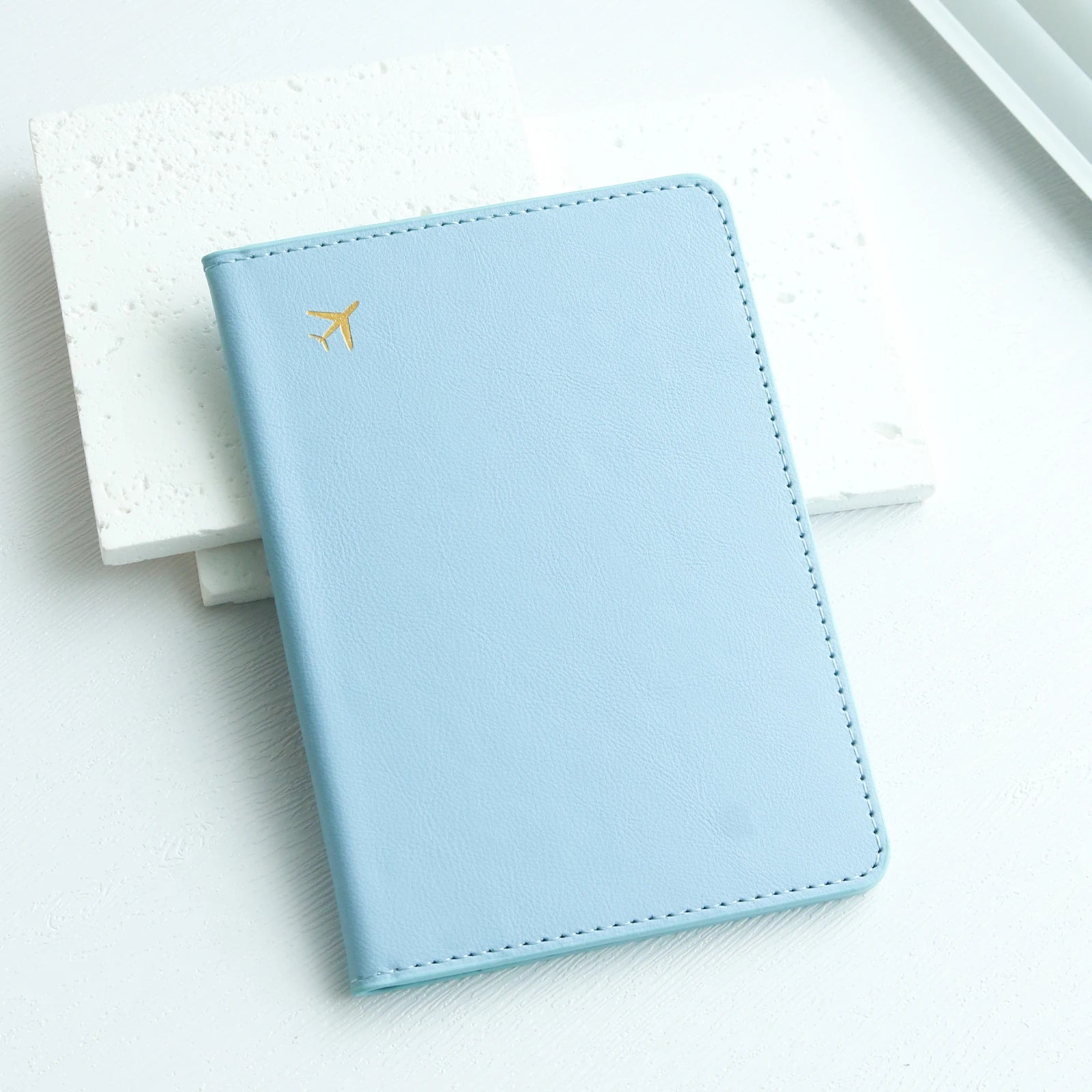 Light blue passport holder with gold airplane icon on white background, Elarose travel accessory